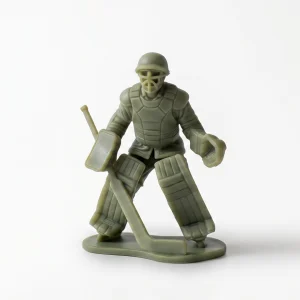 green resin figurine of a WWII-style soldier wearing an M1 helmet and field jacket layered with vintage hockey goalie pads, holding a goalie stick and catching glove,